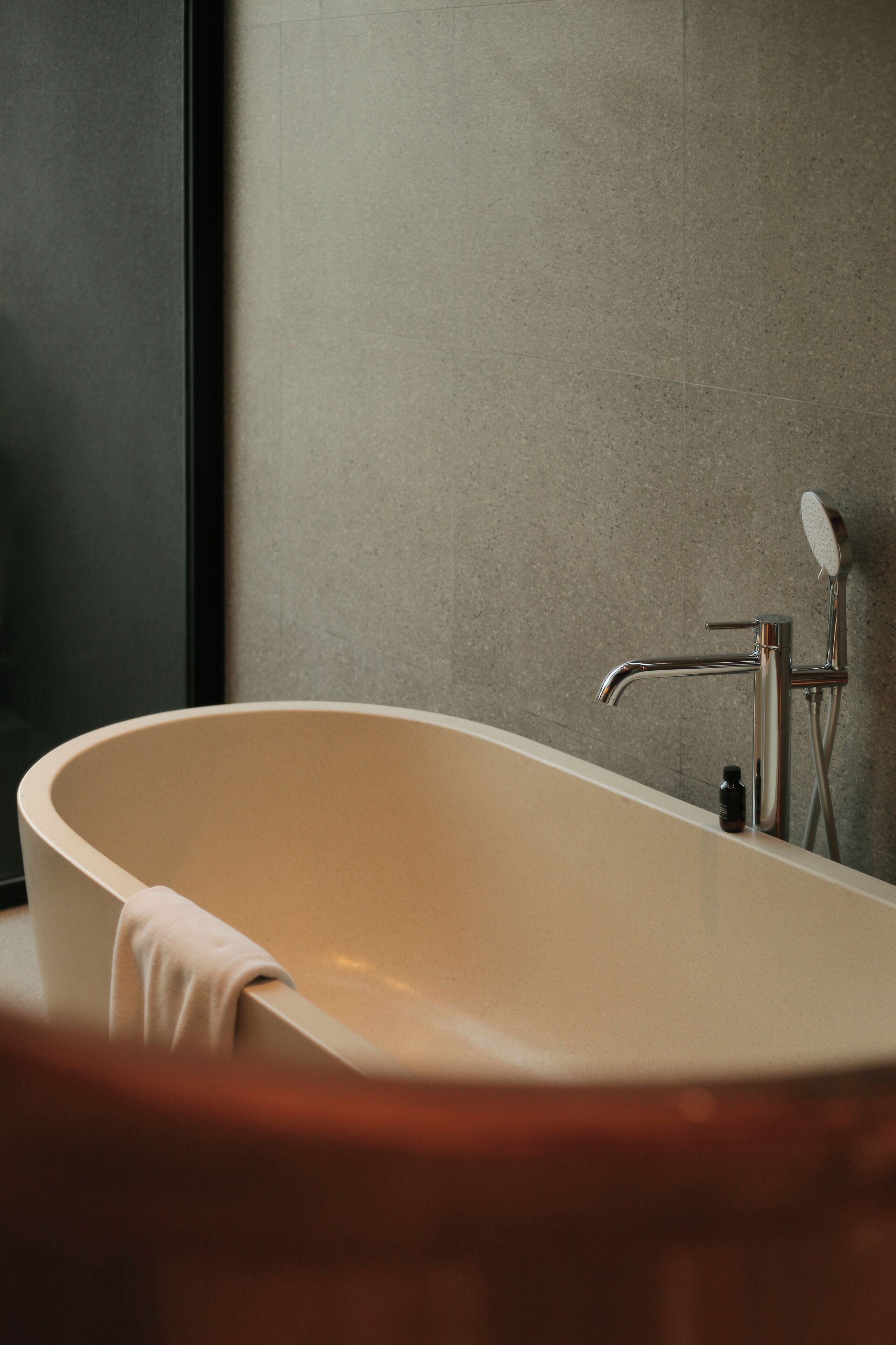 A modern bathroom with a freestanding bathtub, a handheld showerhead, and a small bottle of shampoo on the edge.
