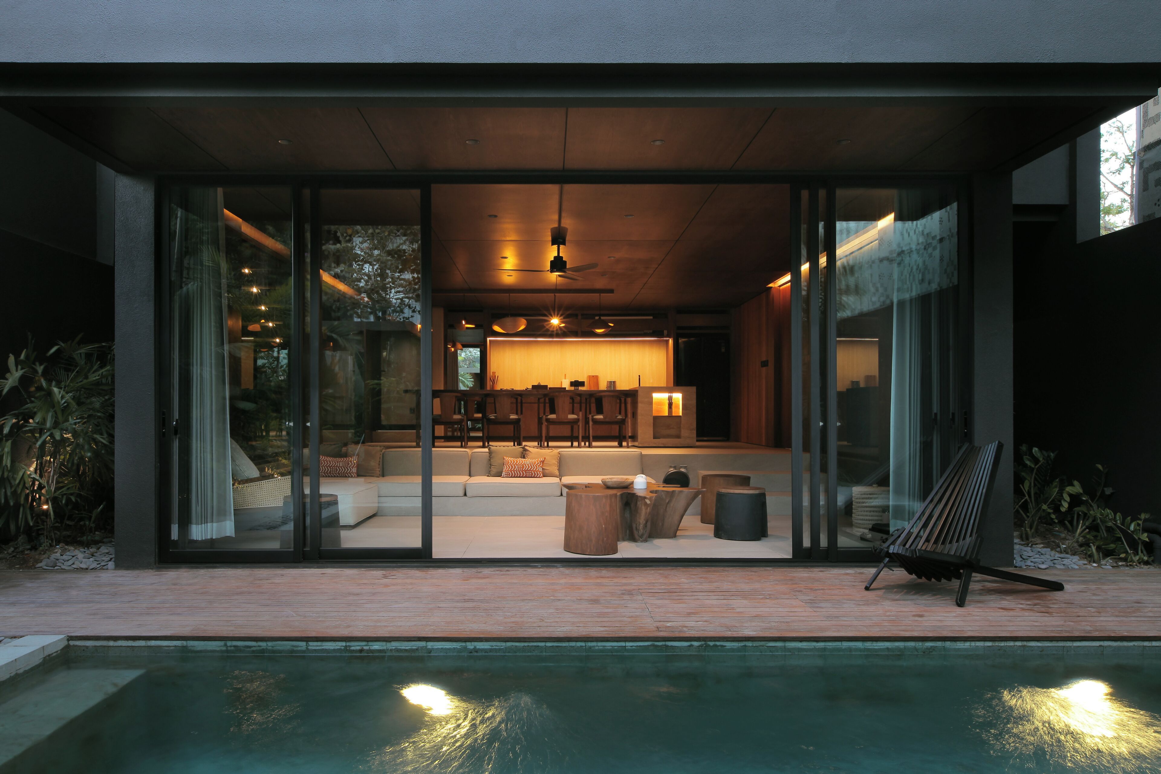 Una casa moderna con fachada de vidrio, una piscina y un comedor con mobiliario de madera.