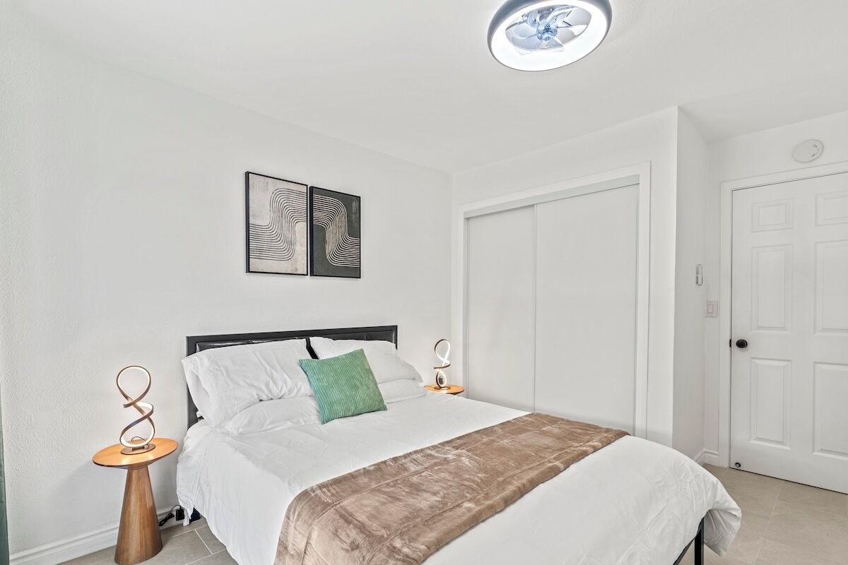 A bedroom with a bed, two bedside tables, a wall-mounted light fixture, and a door.