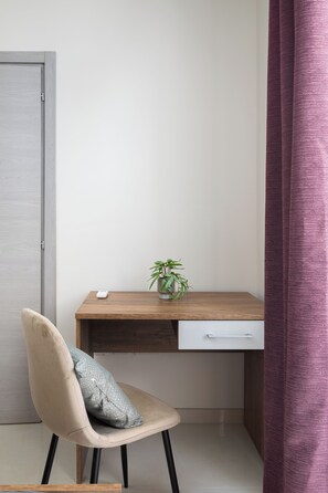 Un bureau d’angle avec un bureau en bois, un tiroir blanc, une petite plante en pot et une chaise avec un coussin.