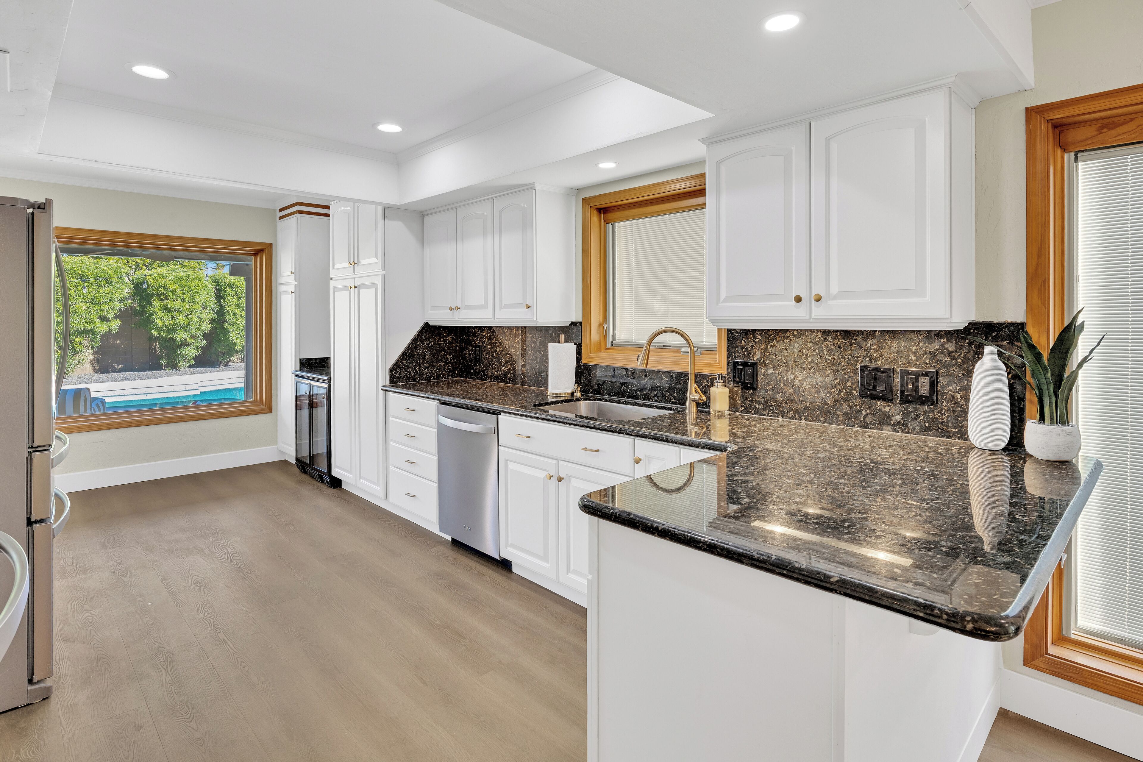 A modern kitchen with white cabinets, granite countertops, and a built-in dishwasher.