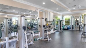 Een fitnessruimte met diverse fitnessapparaten, spiegels en een groot raam met beplanting erbuiten.