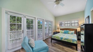 A bedroom with a bed, a chair, a ceiling fan, and large windows with blinds. - OCEAN VIEW ANGLERS REEF - POOL, BEACH. Walk or bike to local food + bars (Islamorada)