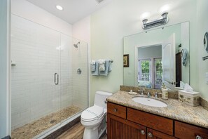 Une salle de bain équipée d’une douche, de toilettes, d’un meuble-lavabo avec un évier et d’un grand miroir.