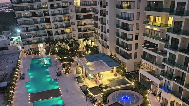 Um hotel moderno com vários andares, área central de piscina com múltiplas piscinas e espaços ao ar livre bem iluminados.