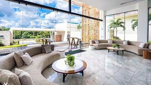 Uma sala de estar moderna com um sofá curvo, uma mesa de centro redonda e janelas amplas que oferecem vista para o exterior.