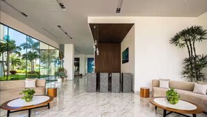 Um lobby moderno com parede de vidro, balcão de recepção e dois sofás com mesinhas de centro.