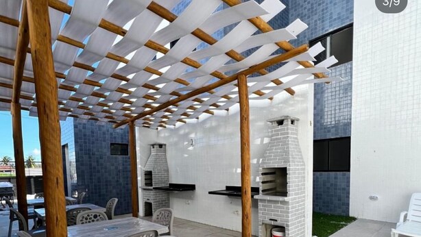 Un espace extérieur aménagé en terrasse, avec des tables et des chaises, une pergola et deux fours en briques.