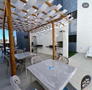 Un espacio de patio al aire libre con mesas y sillas, una estructura de pérgola y dos hornos de ladrillo.