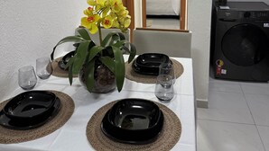 Un coin repas avec une table dressée pour deux personnes, agrémentée d’assiettes noires, de verres transparents et d’un vase contenant des fleurs jaunes.