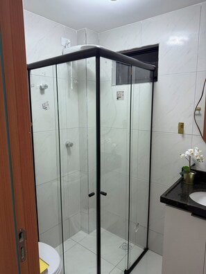 Un baño moderno con ducha de vidrio, inodoro y lavamanos con una pequeña orquídea en maceta.