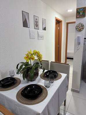 Un comedor con una mesa dispuesta para cuatro personas, paredes blancas y una puerta que da a otra habitación.
