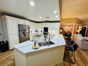 A modern kitchen with white cabinets, a stainless steel refrigerator, and a central island with a sink. - 5BR Retreat Near Downtown | Pets OK | Sleeps 12 (Greeley)