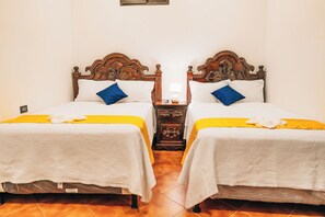 Una habitación con dos camas, cada una con cabecero de madera, una mesita de noche con lámpara y una colcha amarilla.