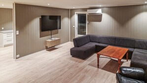 A modern living room with a sectional sofa, a wooden coffee table, a flat-screen TV mounted on the wall, and a sliding door leading to another room. - 4 bedroom beautiful home in Limingen (Limingen)