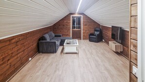 Um quarto de sótão aconchegante com paredes de madeira, um sofá, uma mesa de centro, uma cadeira e uma televisão.
