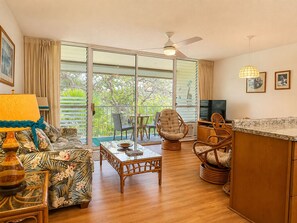 A living room with a sofa, a table, a TV, wicker chairs, and a balcony with a view. - Soothing 1-bedroom condo with AC in lovely Kihei (Kihei)