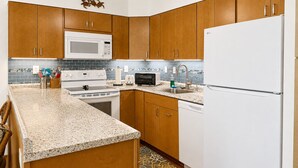 A kitchen with wooden cabinets, a white refrigerator, a microwave, a stove, and a ceiling fan. - Relaxing Kihei Getaway - Walk to Beaches, Dining & Shops (Kihei)