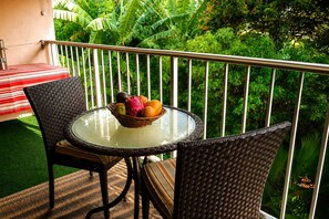 A round glass table with a wicker chair and a wicker chair with a striped cushion. A wicker basket with fruit is on the table. - Soothing 1-bedroom condo with AC in lovely Kihei (Kihei)