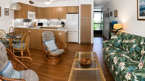 A modern kitchen with wooden cabinets, a dining area with wicker chairs, a glass coffee table, and a floral sofa. - Relaxing Kihei Getaway - Walk to Beaches, Dining & Shops (Kihei)