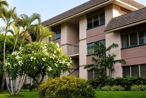 A multi-story building with balconies, surrounded by lush greenery and flowering plants. - Soothing 1-bedroom condo with AC in lovely Kihei (Kihei)