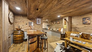 Un interior rústico con paredes de madera, una zona de bar con taburetes, un sofá de cuero y una alfombra de cuero de vaca.