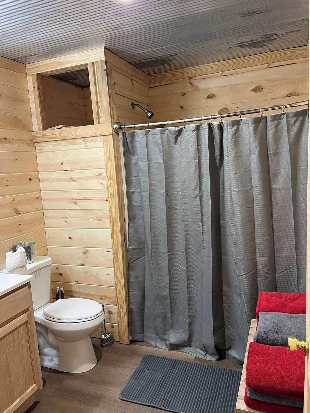 Une petite salle de bain en bois comprenant des toilettes, un rideau de douche et un petit lavabo.