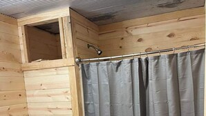 Une petite salle de bain en bois comprenant des toilettes, un rideau de douche et un petit lavabo.