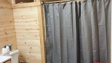 Une petite salle de bain en bois comprenant des toilettes, un rideau de douche et un petit lavabo.