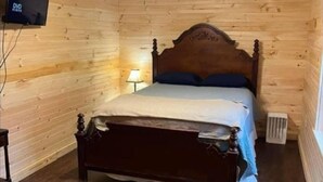 Une pièce aux murs lambrissés, comprenant un lit simple, un ventilateur de plafond, un téléviseur fixé au mur et une petite table.