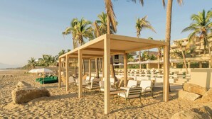 A beachside resort with a covered seating area, lounge chairs, and palm trees. - Anera: Sunset Villa with Terrace & Pool (Playa Blanca)