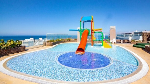 A pool with a slide and play structure, surrounded by a clear blue sky and a view of the ocean. - Beachfront apartment - Resort style (Santa Marta)