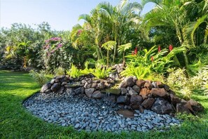 A garden with a rock waterfall, lush greenery, and a variety of tropical plants. - Kihei budget friendly 2 bedroom condo across from beach, AC, walk to everything (Kihei)