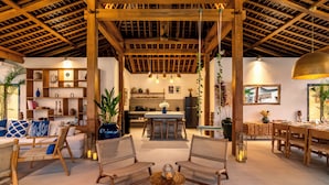 Un'ampia zona giorno con soffitto in legno, una cucina sullo sfondo e un'area pranzo con tavolo e sedie.