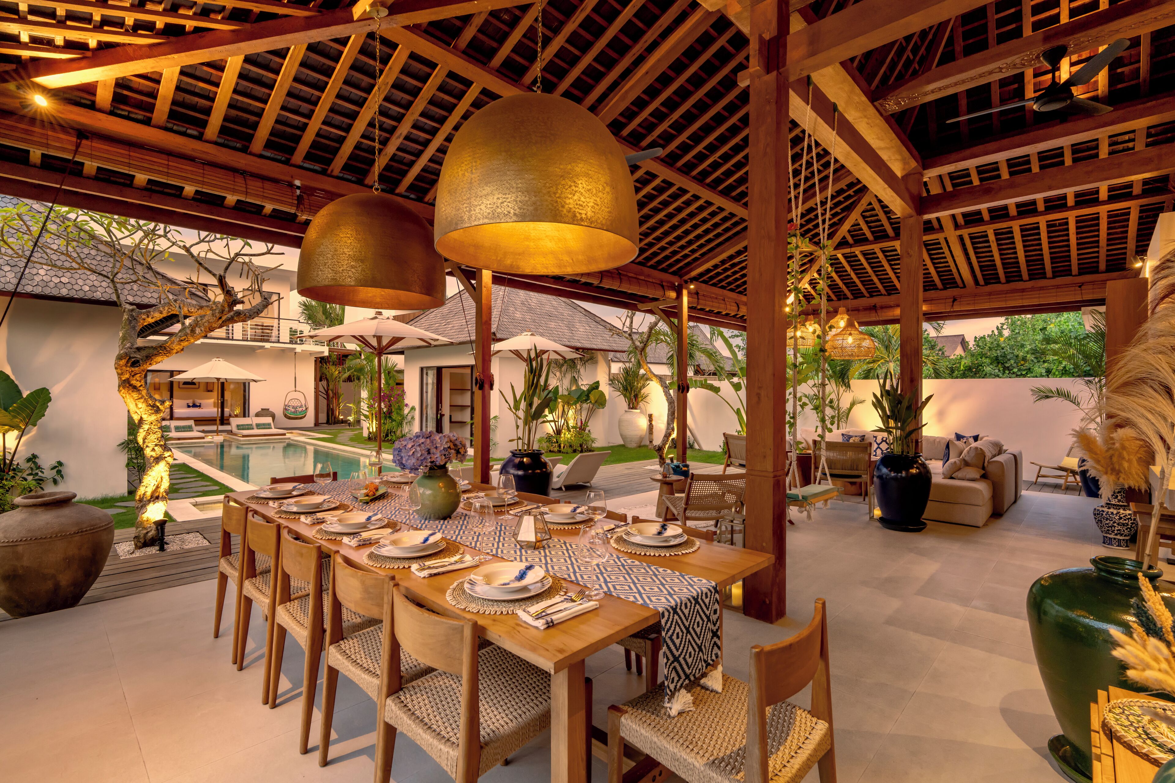A dining area with a pool view, wooden furniture, and hanging pendant lights.