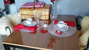 A dining table set with white plates, red napkins, and a red heart-shaped napkin. A wicker basket and a vase with a red rose are on the table. - Cabin in the countryside of Nova Petrópolis, Serra Gaúcha - Chacara Villagio das Pedras (Nova Petrópolis)