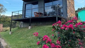 A modern two-story house with a balcony, stone exterior, and a grassy yard. - Cabin in the countryside of Nova Petrópolis, Serra Gaúcha - Chacara Villagio das Pedras (Nova Petrópolis)