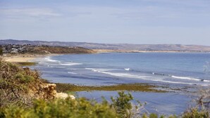 Un paysage côtier avec une plage, l’océan et des collines à l’horizon.