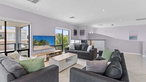 Un salon spacieux doté d’une grande fenêtre, d’un téléviseur à écran plat, d’un canapé, d’une table basse et d’un escalier.