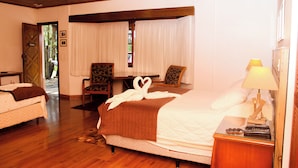 Una habitación de hotel con techo de madera, una cama con manta marrón, un escritorio con silla y una mesita de noche con lámpara.