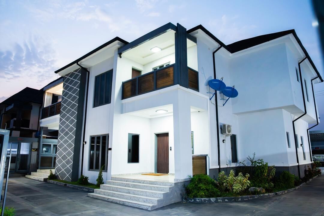 Una casa moderna de dos pisos con balcón, antena parabólica y un jardín bien cuidado.