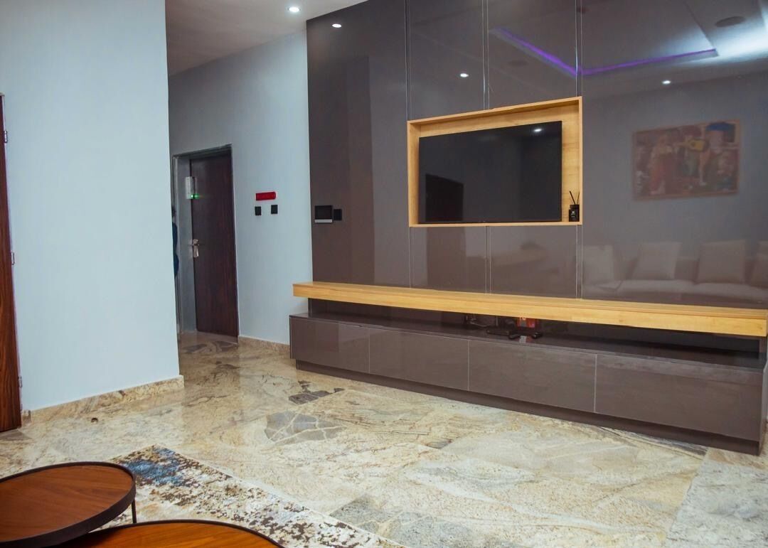 A lobby with a marble floor, a wooden bench, a wall-mounted TV, and a door with a red light.