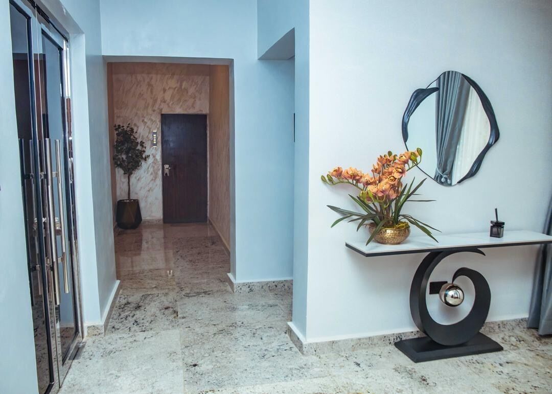 A hallway with a marble floor, a wooden door, a potted plant, and a wall-mounted mirror.