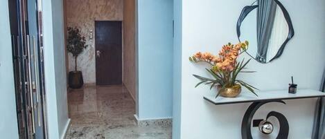 A hallway with a marble floor, a wooden door, a potted plant, and a wall-mounted mirror.