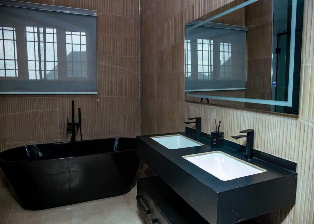 Un baño moderno con dos lavamanos, un espejo grande y una bañera negra.
