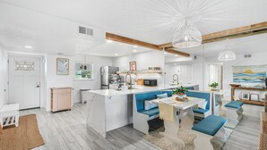 A modern kitchen with white cabinetry, a central island, and blue seating. - Steps to Sand: Ground-Floor Condo with Patio, Private Beach Access & Pool! ☀️ (Satellite Beach)
