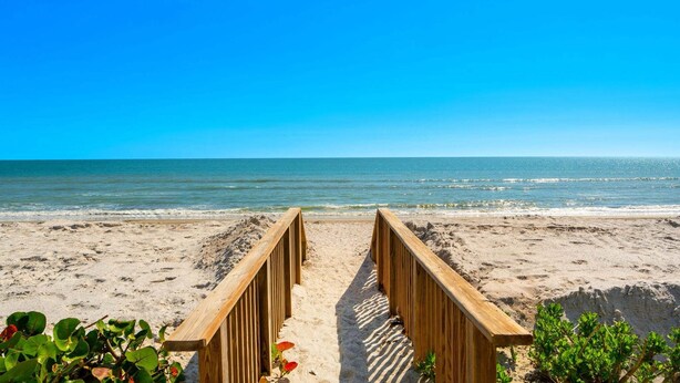A wooden pathway leading to a beach with clear blue skies. - Steps to Sand: Ground-Floor Condo with Patio, Private Beach Access & Pool! ☀️ (Satellite Beach)