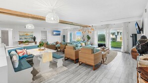 A spacious living room with a large sofa set, a dining table, and a view of the outdoors. - Steps to Sand: Ground-Floor Condo with Patio, Private Beach Access & Pool! ☀️ (Satellite Beach)
