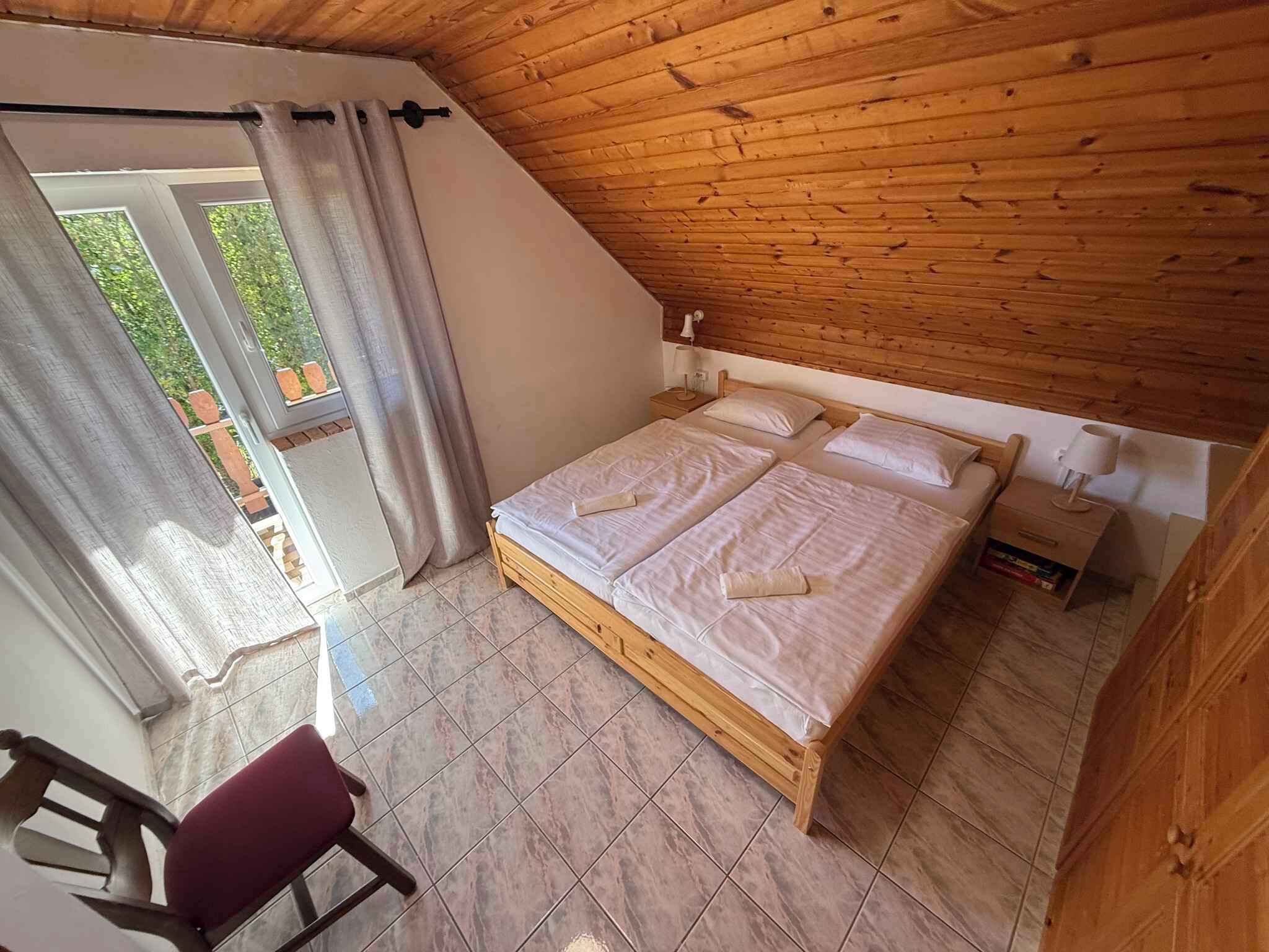 Une chambre avec un plafond en bois, un lit recouvert de draps blancs, une table de chevet avec une lampe et une chaise.