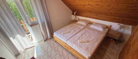 Une chambre avec un plafond en bois, un lit recouvert de draps blancs, une table de chevet avec une lampe et une chaise.